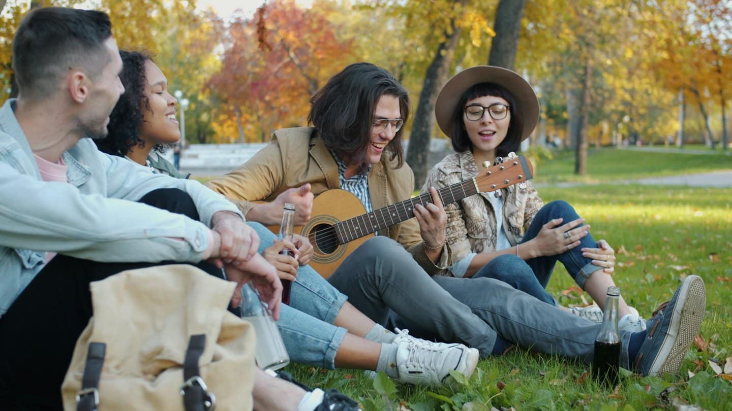 Amigos tocan música y cantan en el césped en otoño.