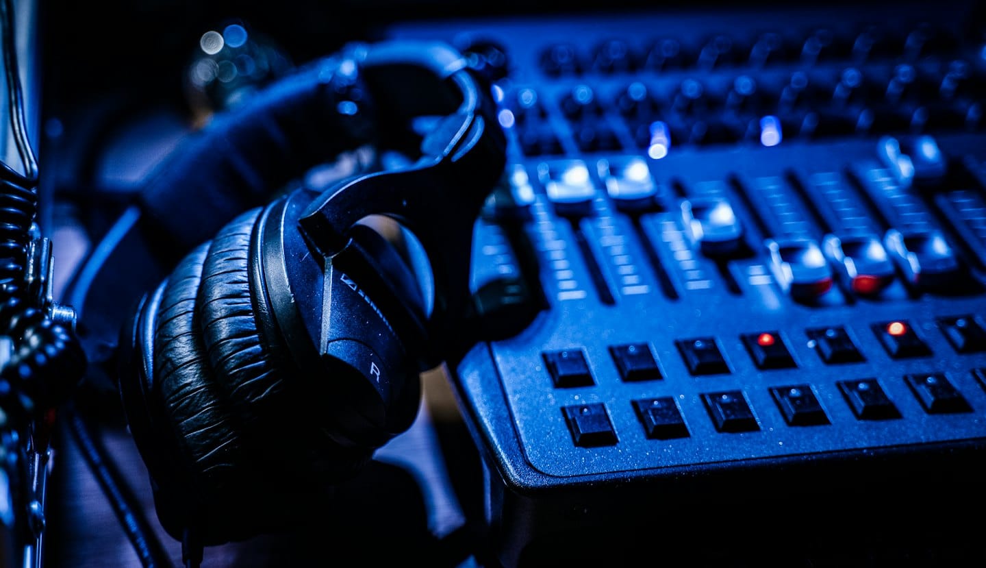 Auriculares negros sobre una mesa de mezclas de audio con luz azul.