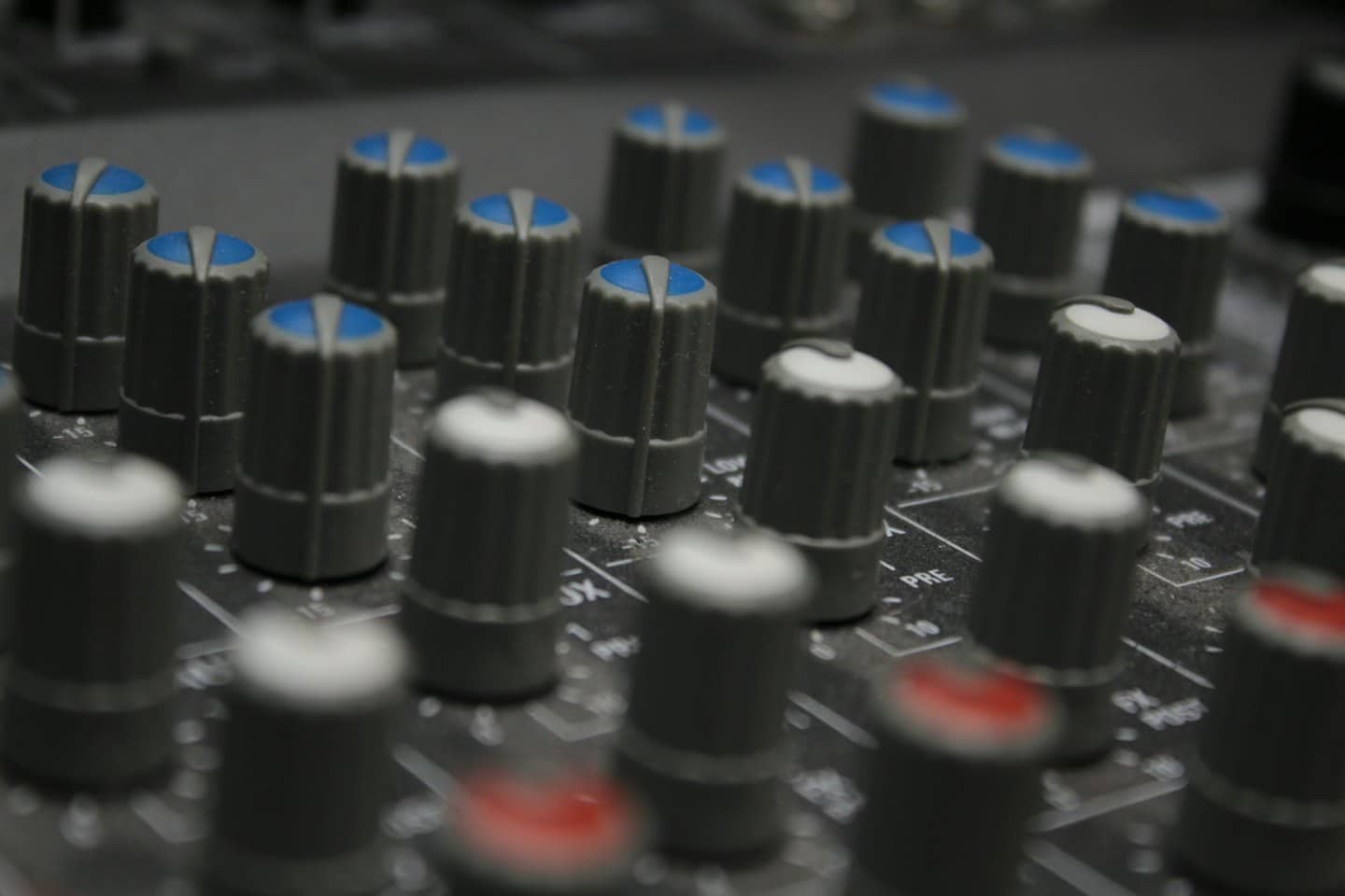 Consola de mezcla de audio con muchas perillas grises e indicadores de colores.